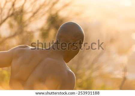 African american black male model standing topless with no shirt, showing muscular fit body at sunrise in long grass and bush
