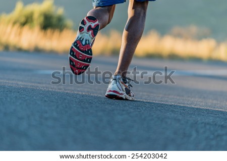 Closeup of an athlete runner\'s feet and shoes running along a road outdoors with a mountain background. Men fitness during sunrise jogging