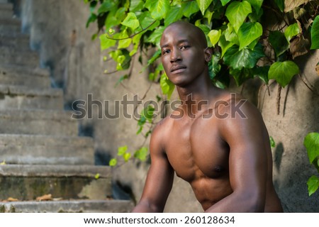 Sad black, african american man, crouched while thinking against a green plant and concrete wall, wearing no shirt