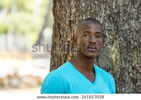 African american black man with blue shirt, standing in park, next to a tree in a park during summer
