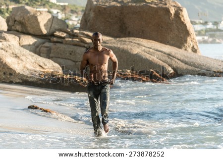 Black man running along the beach, splashing water