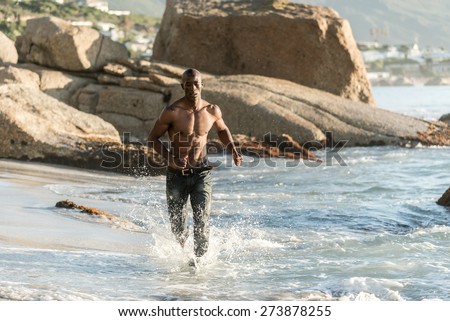 Black man running along the beach, splashing water