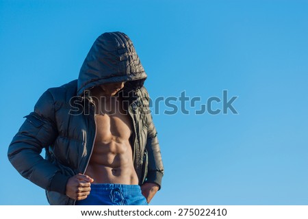 Fit, athletic and muscular African  male wearing black bomber jacket hoodie with zipper, isolated with blue sky