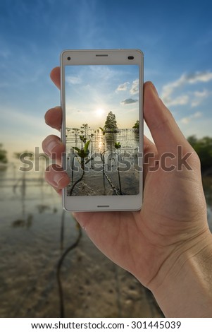 Tourist hand holding smart phone, taking photo of Thailand beach sunset