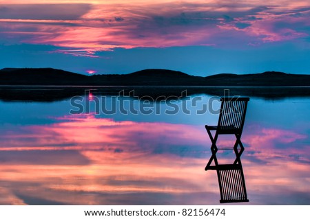 Scenic view of sunset over inlet and hills with a chair in the calm water, with reflections of sunset and chair. Symbolizing peace, loneliness or emptiness
