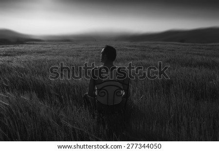 man sitting on a chair in a field of wheat black and white photography