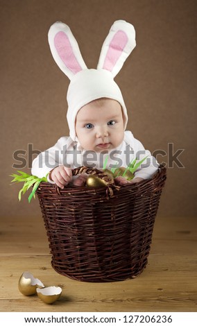 Little baby dressed as a bunny sitting in a wicker basket, which is full of golden eggs. Good as an Easter greetings.