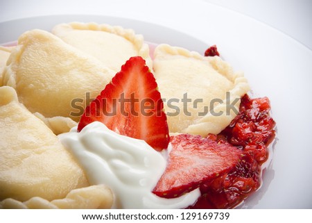 Varenyky or pierogy stuffed with cottage cheese, served with sour cream and strawberry sauce. A traditional Ukrainian or Polish dessert.