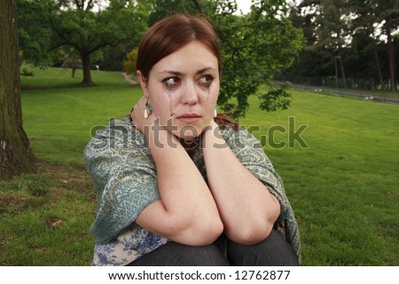 A girl in tears. Emotions of a young woman sitting alone in a garden.