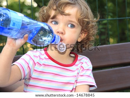 The little girl is drinking water from the plastic bottle.