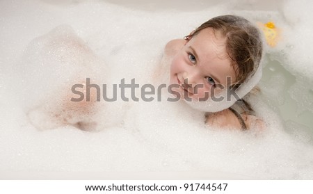 Little girl having fun in a bathtub full of soap foam.