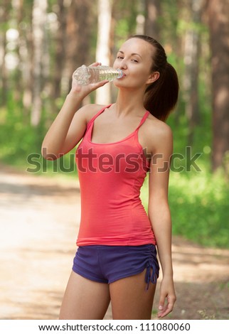 Fitness woman drinking water from bottle outdoors