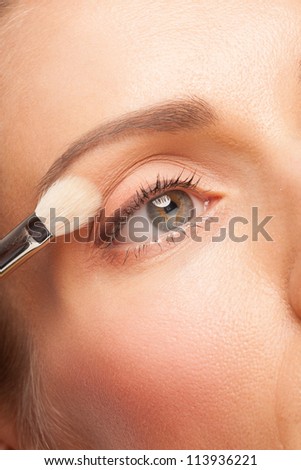 Closeup shot of woman applying eyeshadow on eyelid using makeup brush