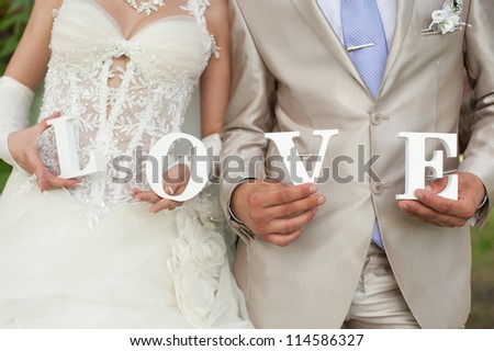 Closeup shot of bride and groom hands holding the word Love