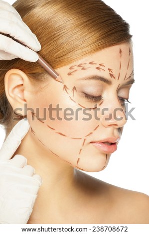 Beautiful young caucasian woman with perforation lines on her face before plastic surgery operation. Beautician touching woman face.