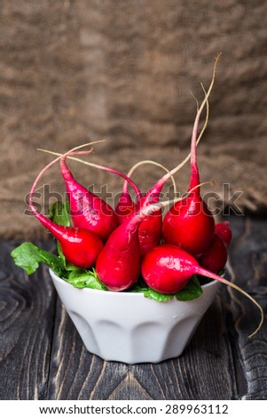 Red organic radishes in white bowl on wooden rustic table