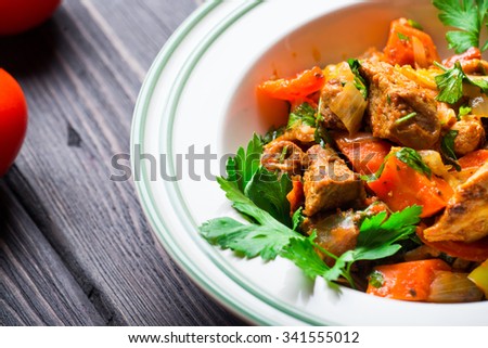 Meat stew with vegetables and herbs on dark wooden background