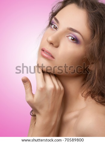 Attractive female with make-up touching her face and looking away, over pink background