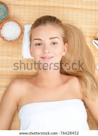 Beautiful woman with long blond hair lying on bamboo mat at spa salon and relaxing