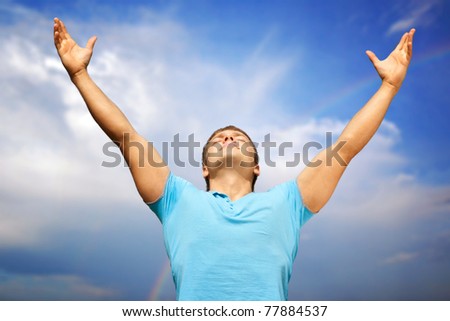 Happy young man with raised arms and closed eyes against blue sky