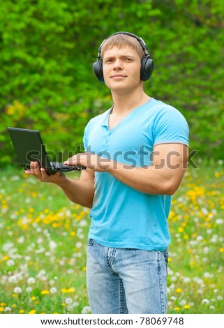 Young man working with a laptop and listening music on headphone outdoors