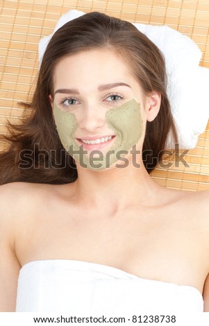 Close-up of young beautiful woman with clay facial mask at spa salon
