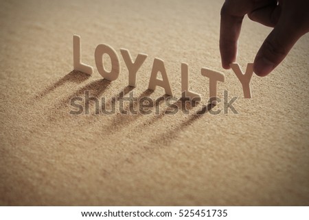 LOYALTY wood word on compressed board with human\'s finger at Y letter