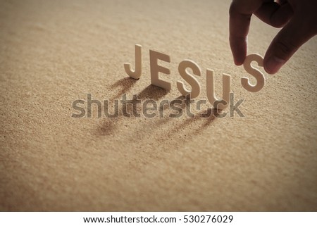 JESUS wood word on compressed board with human's finger at S letter