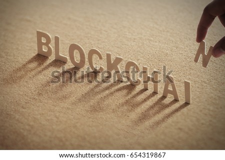 BLOCKCHAIN wood word on compressed or corkboard with human\'s finger at T letter.