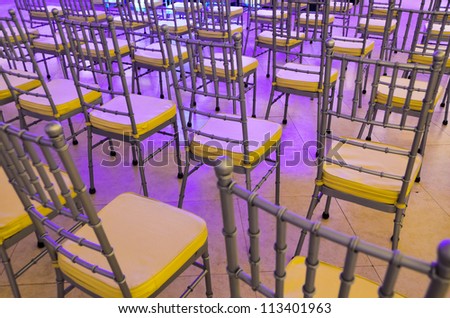 Rows of event chairs for guests and audience bathe in purple stage lights