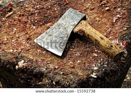 Axe used by butchers on big chopping board scattered with bits and pieces of livestock meat