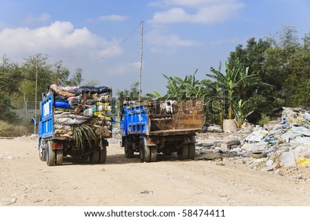 One garbage truck overflowing with trash in old sacks; other truck is empty
