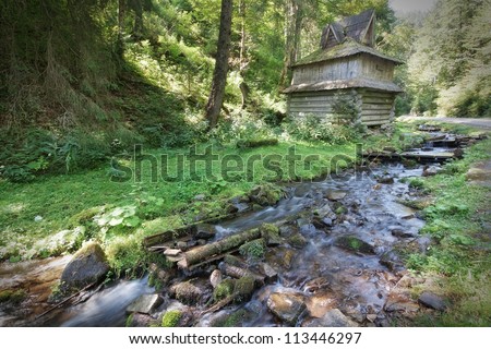 Mountain forest stream flows near the wooden house.