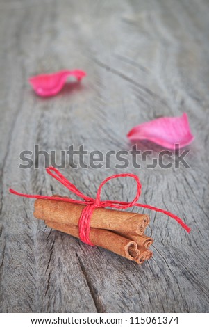 Canela sticks on the background rose petals on wooden texture.