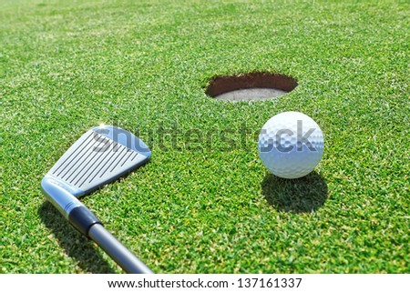 Golf stick and ball on the grass near the hole.