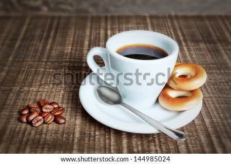 A cup of coffee with baked cracknels, bagels. Coffee beans on the wooden background.