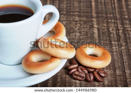 A cup of coffee with baked bagels, close-up. Coffee beans on the wooden background.
