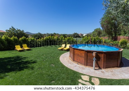 An above ground pool sets on a concrete pad in the backyard on a sunny summer day.