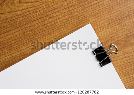 Black clip and blank paper on wooden desk
