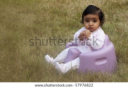 Baby Girl Sitting In a Lawn Surrounded by Dry Green Grass