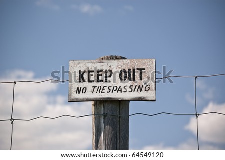 A weathered sign nailed to a fencepost that reads: Keep Out - No Trespassing. Black letters on white sign.
