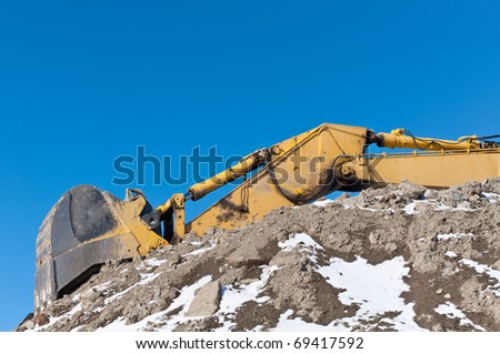 The arm and bucket of a hydraulic excavator on top of a pile of earth in winter.
