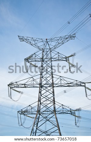 A transmission tower carrying high-voltage electrical lines stands against a blue sky.