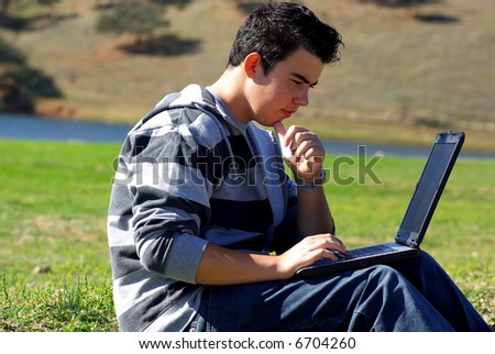 Young teen laptop man at countryside next to water.