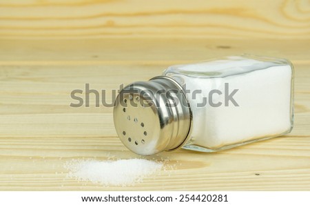 A glass salt shaker with metal lid and spilled salt