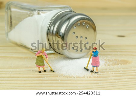 Miniature toy housewives figures cleaning up spilled salt on wooden table