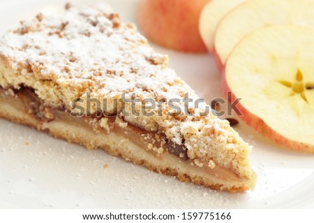 A slice of delicious apple pie with apple slices in the back