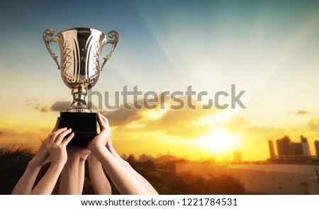 Winning team raise trophy cup with background of sky of light ray