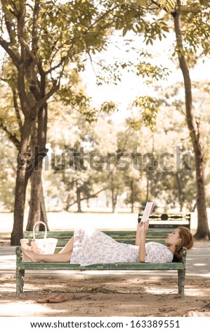 Beautiful Vintage girl reading book in park lying on park chair
