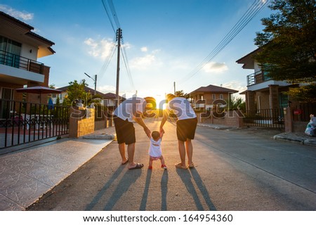 Parents escourting their child to walk together in street at sun